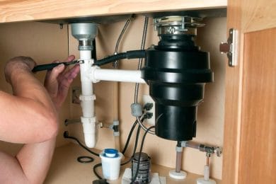 Plumber repairing a garbage disposal beneath a kitchen sink in Horsham